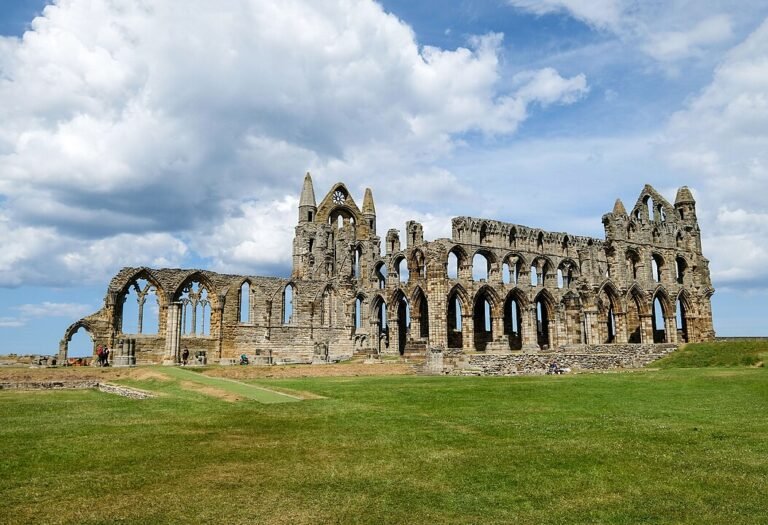 a stone building with arches and a green field with Whitby Abbey in the background