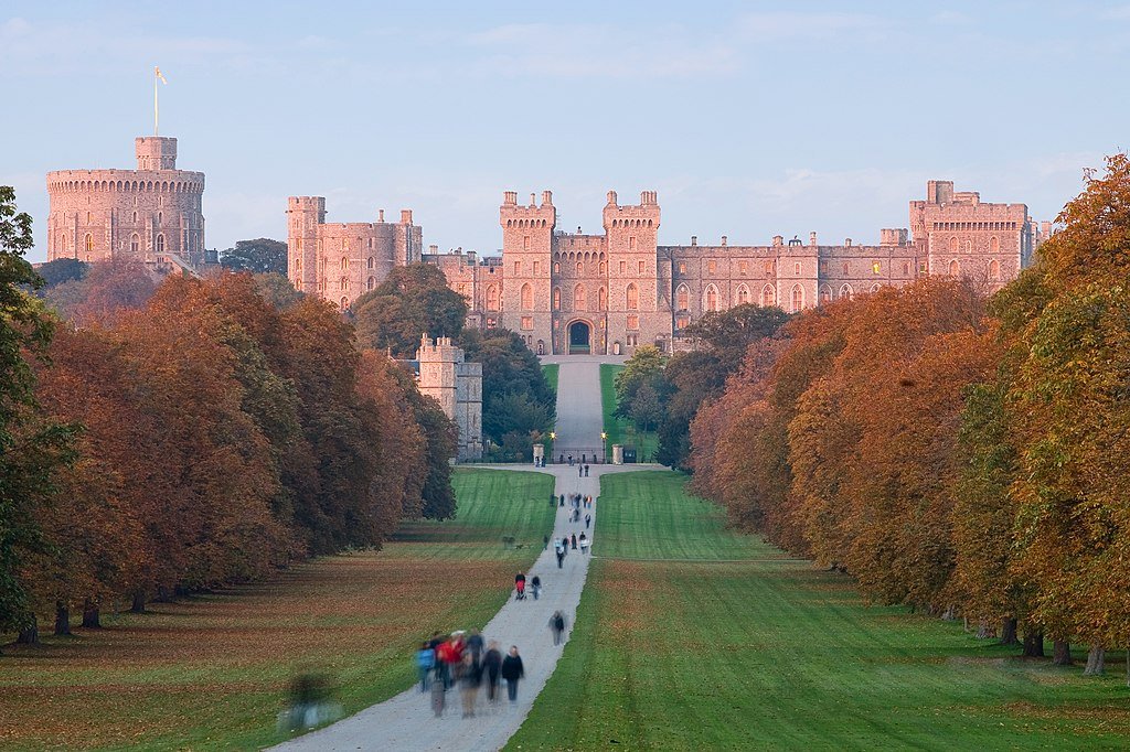 Windsor Castle: A Long pathway lined with autumn-coloured trees leading to a large historic castle with multiple towers under a clear sky